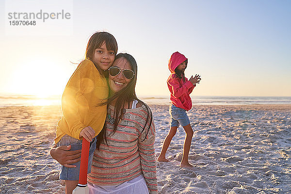 Porträt einer glücklichen Mutter und ihrer Töchter am sonnigen Strand bei Sonnenuntergang