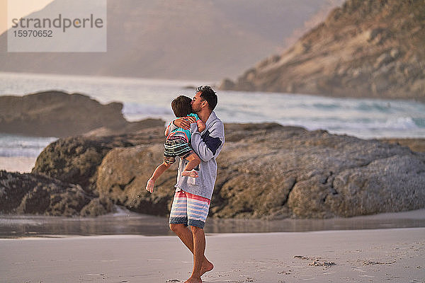 Zärtlicher Vater umarmt und küsst Sohn am Meeresstrand