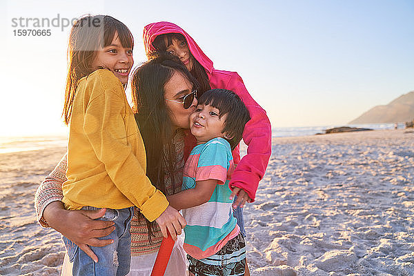 Zärtliche Mutter küsst Kinder am sonnigen Strand