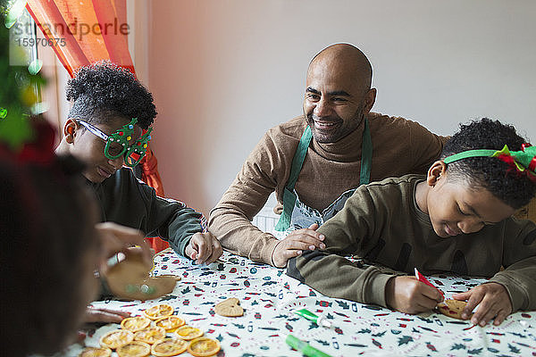 Glückliche Vater und Söhne schmücken Weihnachtsplätzchen bei Tisch