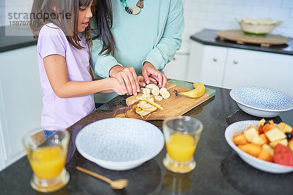 Mutter und Tochter schneiden Bananen in der Küche