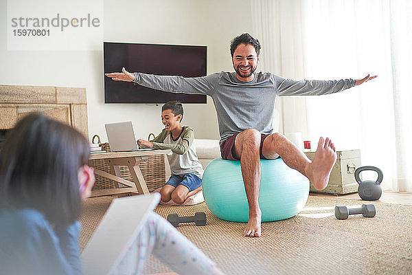Spielerischer Vater übt mit Kindern auf dem Fitnessball im Wohnzimmer