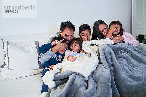 Glückliche Familie schaut Gruselfilm auf Wohnzimmersofa