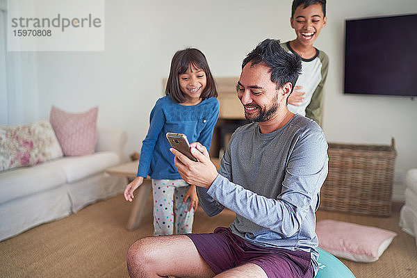 Glücklicher Vater und Kinder mit Smartphone im Wohnzimmer