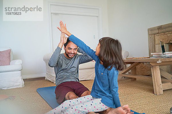 Glücklicher Vater und Tochter High-Five auf Yogamatte im Wohnzimmer