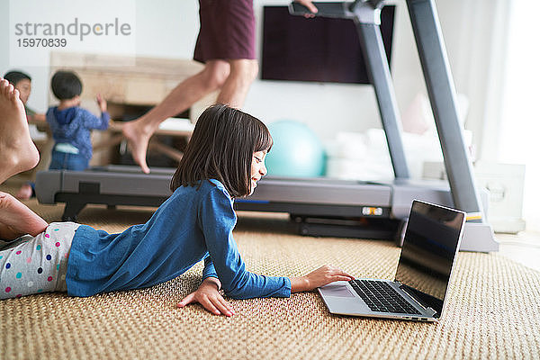 Mädchen benutzt Laptop auf dem Boden neben dem Vater auf dem Laufband