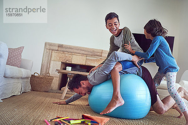 Glückliche Familie spielt im Wohnzimmer auf dem Fitnessball