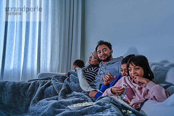Porträt eines glücklichen Mannes  der sich entspannt und mit der Familie auf dem Sofa einen Film schaut