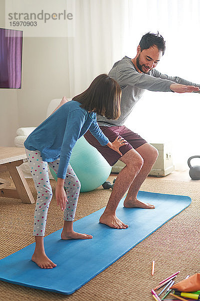 Vater und Tochter üben auf der Matte im Wohnzimmer