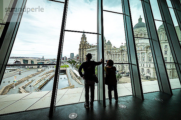 Ein Ehepaar blickt aus den großen Fenstern des Museum of Liverpool auf den Pier Head und das Liver Building  Liverpool  Merseyside  England  Vereinigtes Königreich  Europa
