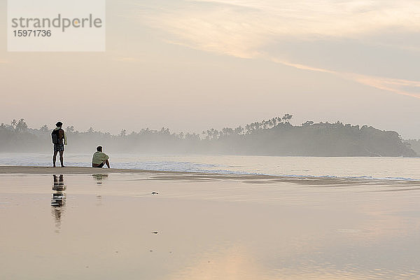 Zwei Männer beobachten den Sonnenaufgang am Strand von Talalla  Sri Lanka  Asien