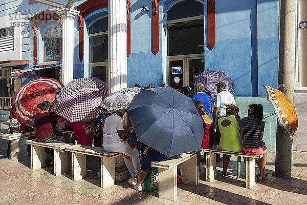 Menschen in einer Warteschlange vor einem Lebensmittelgeschäft  die Regenschirme als Sonnenschirme benutzen  Manzanillo  Kuba  Mittelamerika