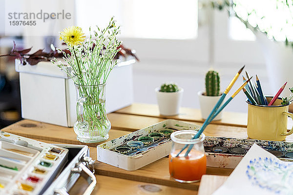 Aquarellfarben mit Blumenvase und Pinseln auf Holztisch zu Hause