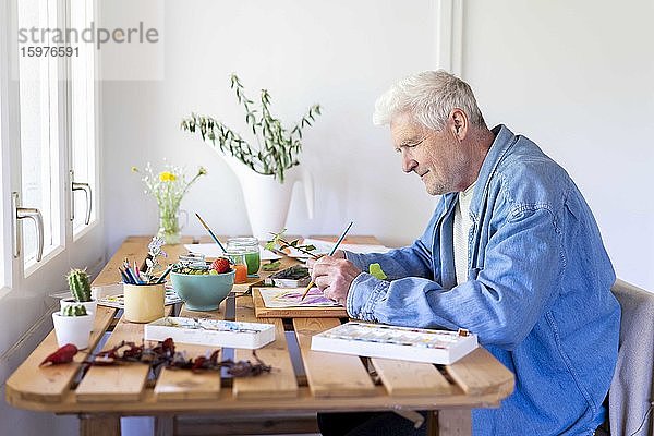 Älterer Mann malt auf dem Tisch zu Hause