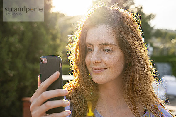 Porträt einer lächelnden rothaarigen Frau  die ihr Smartphone überprüft