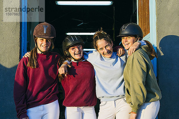 Porträt von fröhlichen weiblichen Jockeys  die an einem sonnigen Tag zusammen vor einem Stall stehen