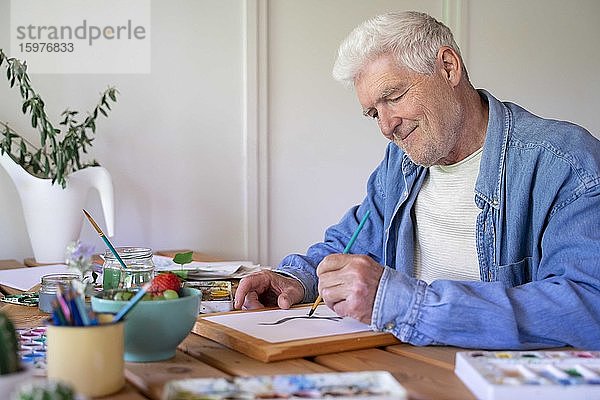 Glücklicher älterer Mann malt auf Papier am Tisch