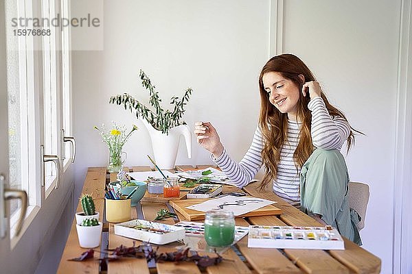 Glückliche junge Frau malt mit Aquarellfarben auf dem Tisch zu Hause