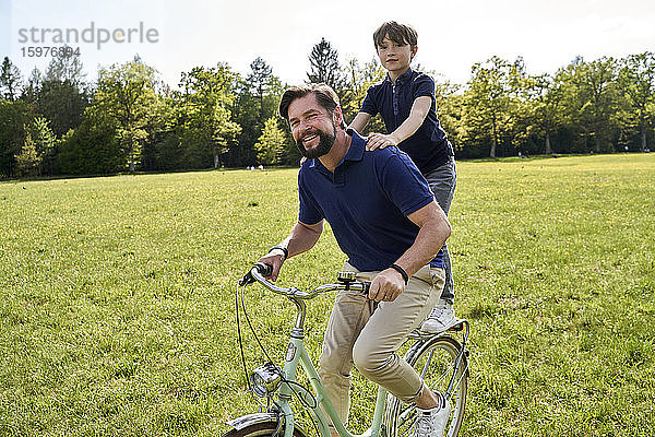 Lächelnder Vater und Sohn genießen eine Fahrradtour im Gras an einem sonnigen Tag