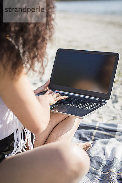 Crop Ansicht der jungen Frau sitzt auf einer Decke am Strand mit Laptop