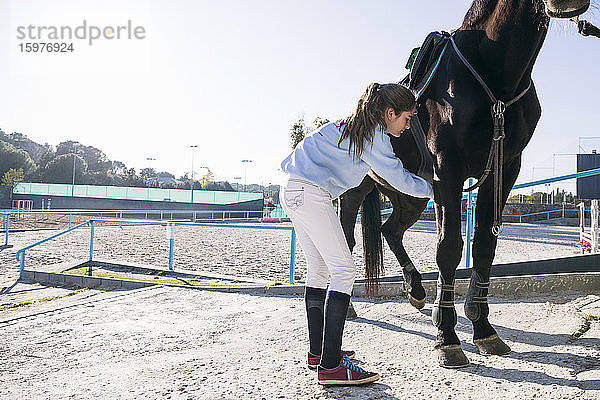 Junges Mädchen legt Ausrüstung an  während sie ihr Pferd auf dem Trainingsplatz vorbereitet