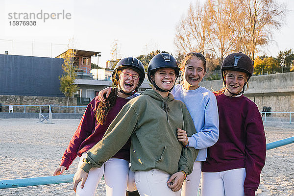 Porträt von fröhlichen weiblichen Jockeys  die auf dem Trainingsplatz gegen den Himmel zusammenstehen