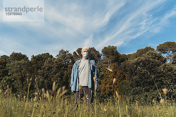 Älterer Mann mit Schutzmaske auf einer Wiese stehend