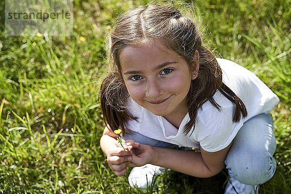 Nettes Mädchen hockt und hält eine kleine gelbe Blume an einem sonnigen Tag