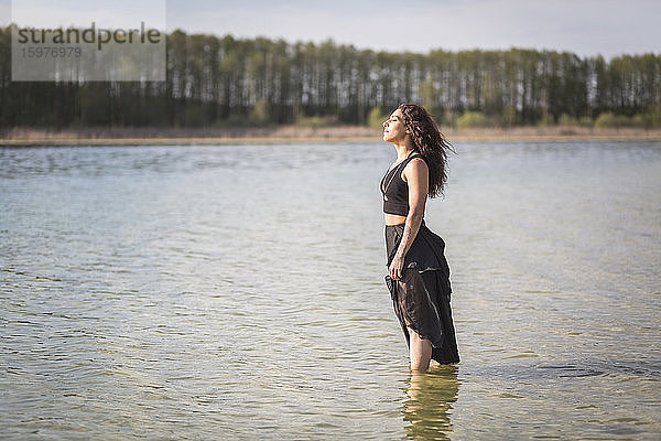 Junge Frau steht im See und genießt das Sonnenlicht  Brandenburg  Deutschland