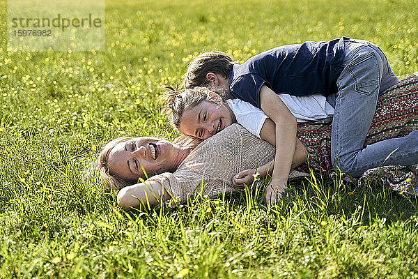 Fröhliche Frau mit Kindern auf ihr liegend an einem sonnigen Tag