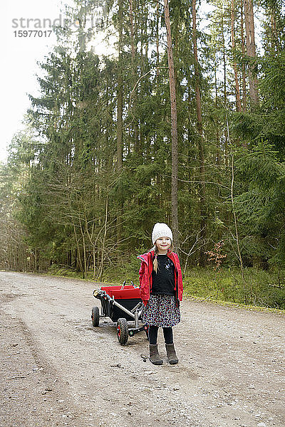Kleines Mädchen mit Draisine auf Waldweg stehend