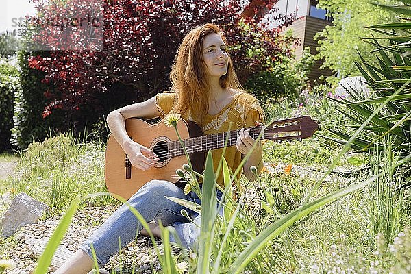Lächelnde junge Frau spielt Gitarre in der Natur