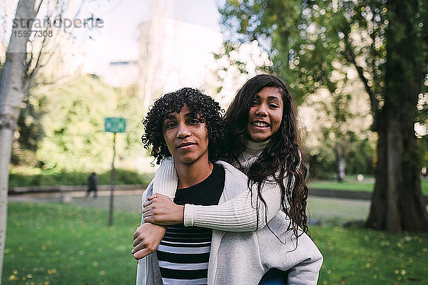 Junge mit lockigem Haar nimmt lächelnde Schwester im Park huckepack