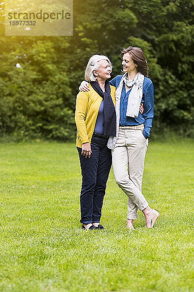 Glückliche ältere Frau und erwachsene Tochter stehen auf einer Wiese in einem Park und schauen sich an