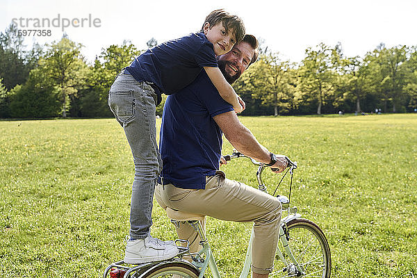 Glücklicher Junge  der seinen Vater umarmt  während er eine Fahrradtour an einem sonnigen Tag genießt