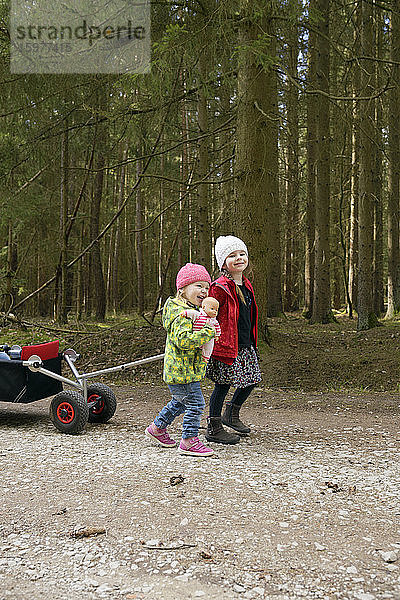 Zwei kleine Schwestern ziehen eine Draisine auf einem Waldweg