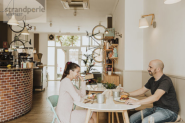 Lächelnder Mann und lächelnde Frau sitzen am Tisch in einem Café
