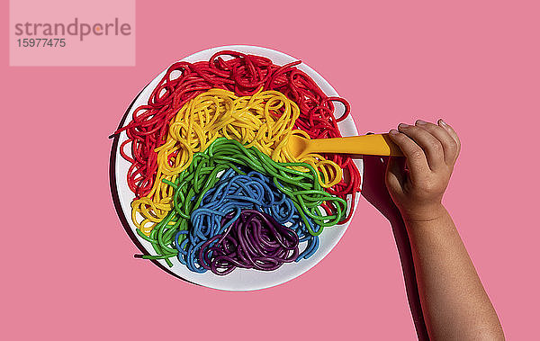 Hand eines kleinen Mädchens  das regenbogenfarbene Spaghetti isst