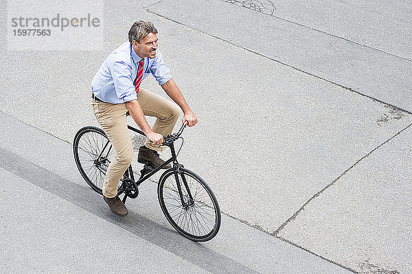 Lächelnder Geschäftsmann fährt Fahrrad auf der Straße in der Stadt