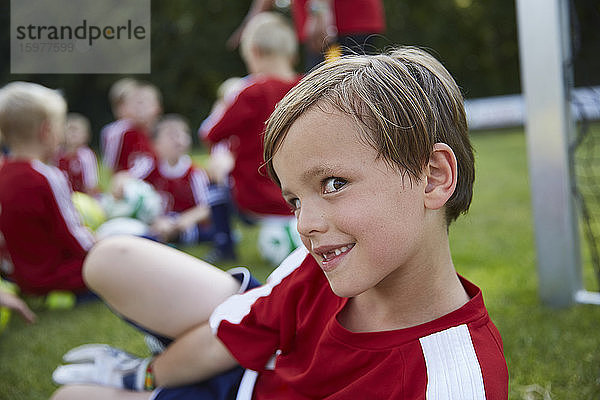 Porträt eines verspielten Jungen mit einer Fußballmannschaft im Hintergrund auf einem Feld