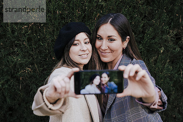 Porträt von zwei lächelnden Frauen  die ein Selfie mit einem Smartphone machen