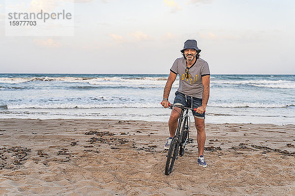 Älterer Mann sitzt auf seinem Fahrrad am Strand