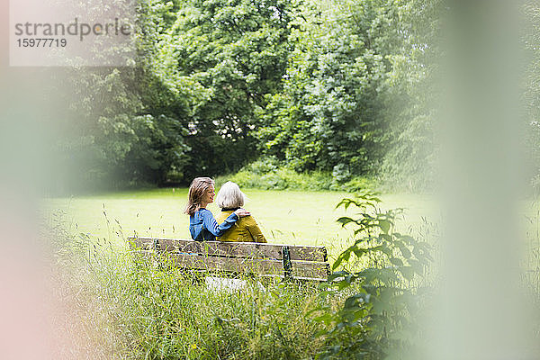 Ältere Frau und erwachsene Tochter sitzen zusammen auf einer Parkbank