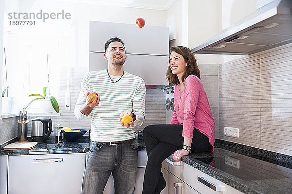 Glückliche Frau sieht Mann an  der in der Küche mit Früchten jongliert