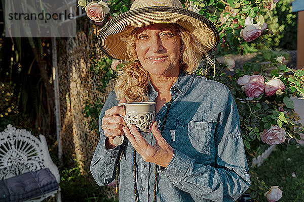 Porträt einer lächelnden älteren Frau mit einer Tasse Tee in ihrem Garten