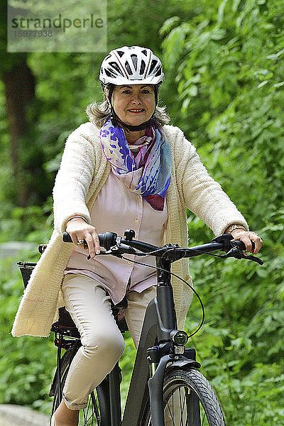 Glückliche ältere Frau fährt mit dem Elektrofahrrad auf dem Fußweg im Park
