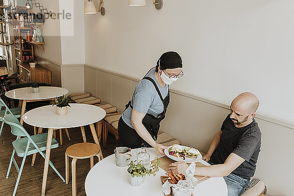 Kellnerin mit Schutzmaske serviert Essen in einem Café