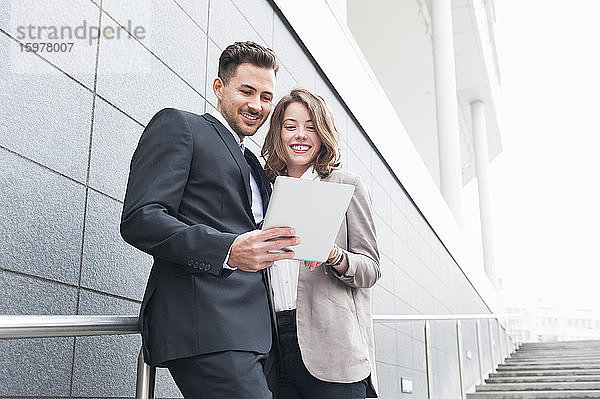 Glückliches Geschäftspaar benutzt ein digitales Tablet  während es auf einer Treppe steht