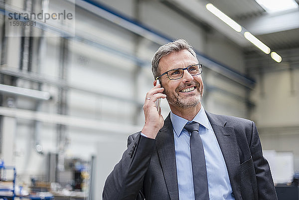 Lächelnder Geschäftsmann am Telefon in einer Fabrik