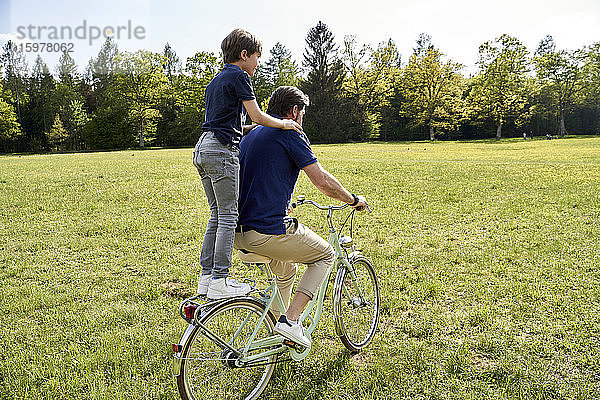 Vater und Sohn genießen eine Fahrradtour im Gras an einem sonnigen Tag